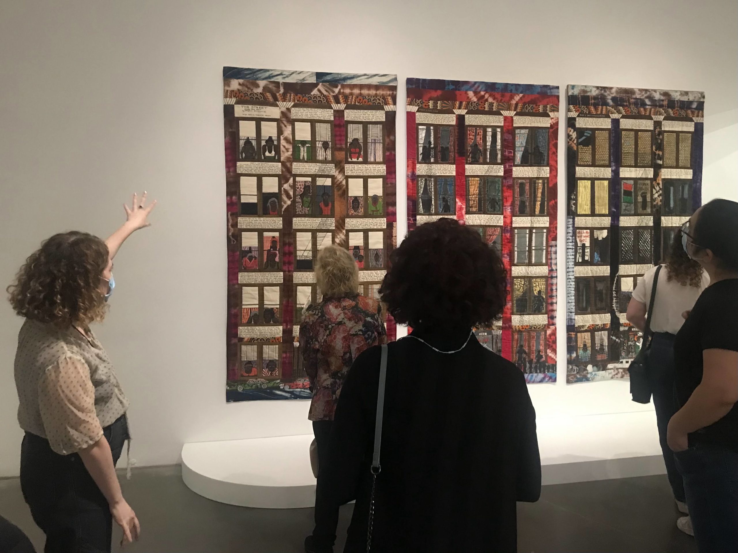 Curator Madeline Weisburg gestures to a tapestry by Faith Ringgold