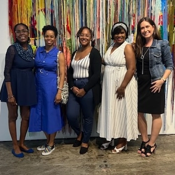 5 women pose for a photo in front of a colorful artwork