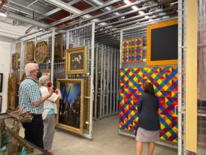 The interior of an art storage area. Several artworks hang on rows of large metal grids.