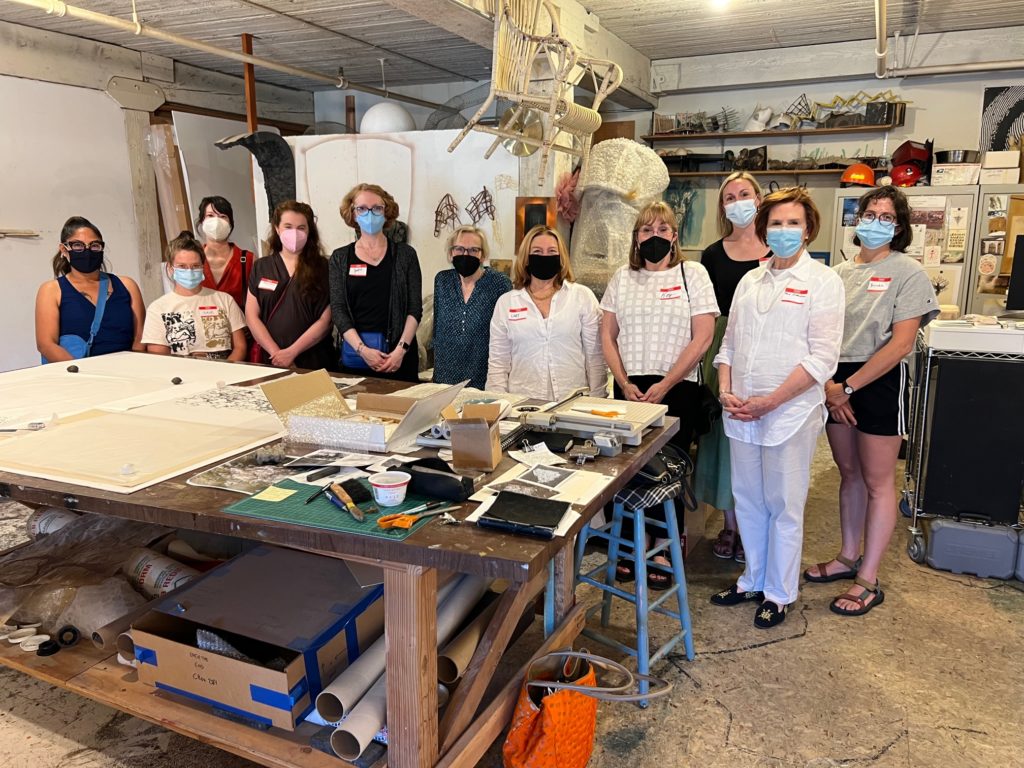 About 10 women pose for a photo inside an artist studio. They all wear face masks.