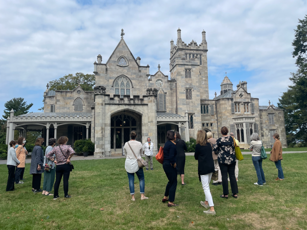 A group gathers outside the Lyndhurst Mansion, a medieval-looking structure, while a guide speaks.